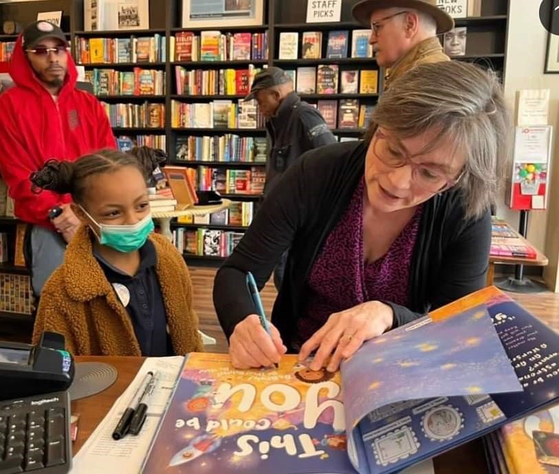 Image of children's book author Cindy William's Schrauben signing her picture book This Could be You with a child watching.